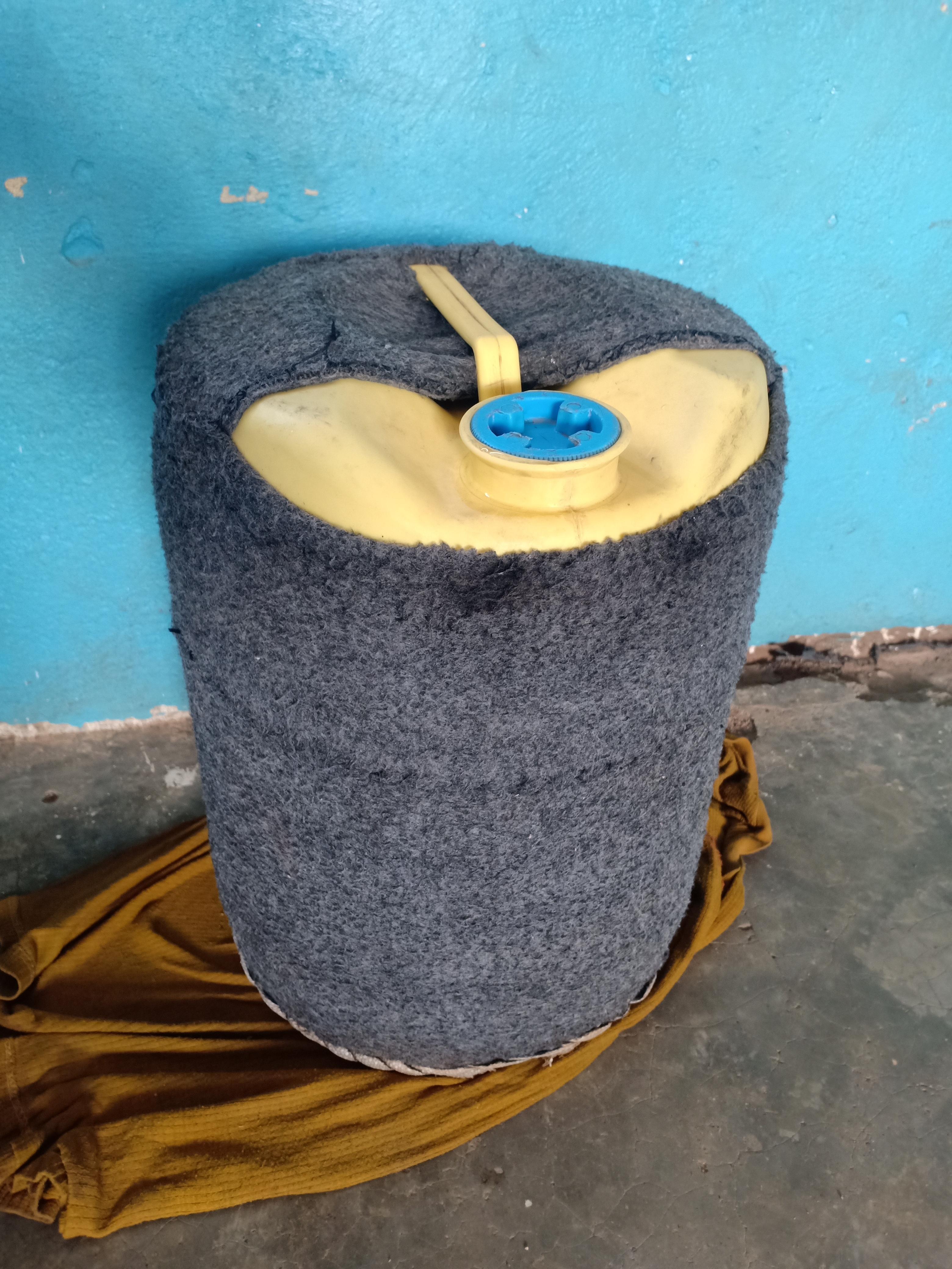 Gray insulated water container with blue cap resting on yellow fabric against a blue wall.